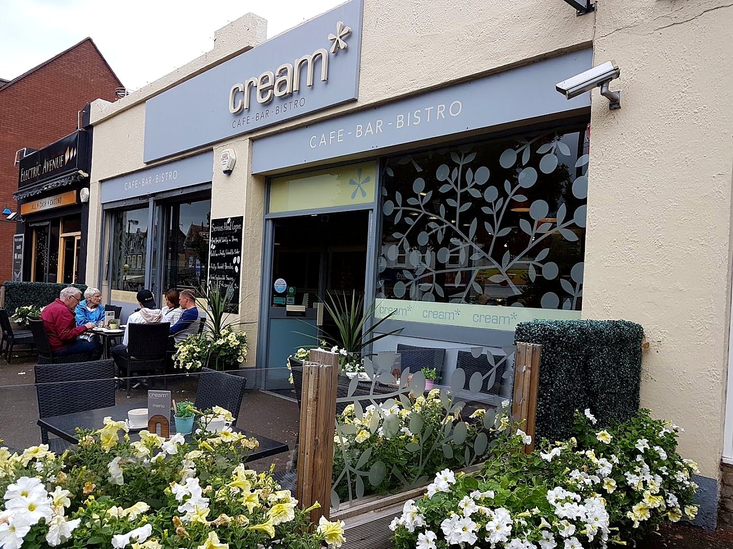 The front of Cream on The Avenue: grey fascia with the name in lowercase, leaf-pattern window, tables and flower boxes outside